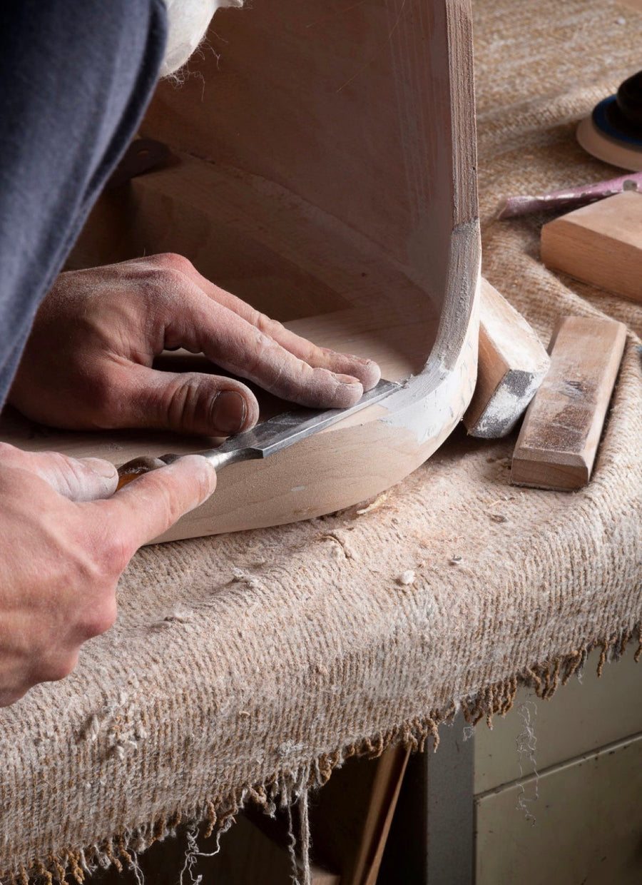 A craftsman shaping a curved frame by hand with a chisel
