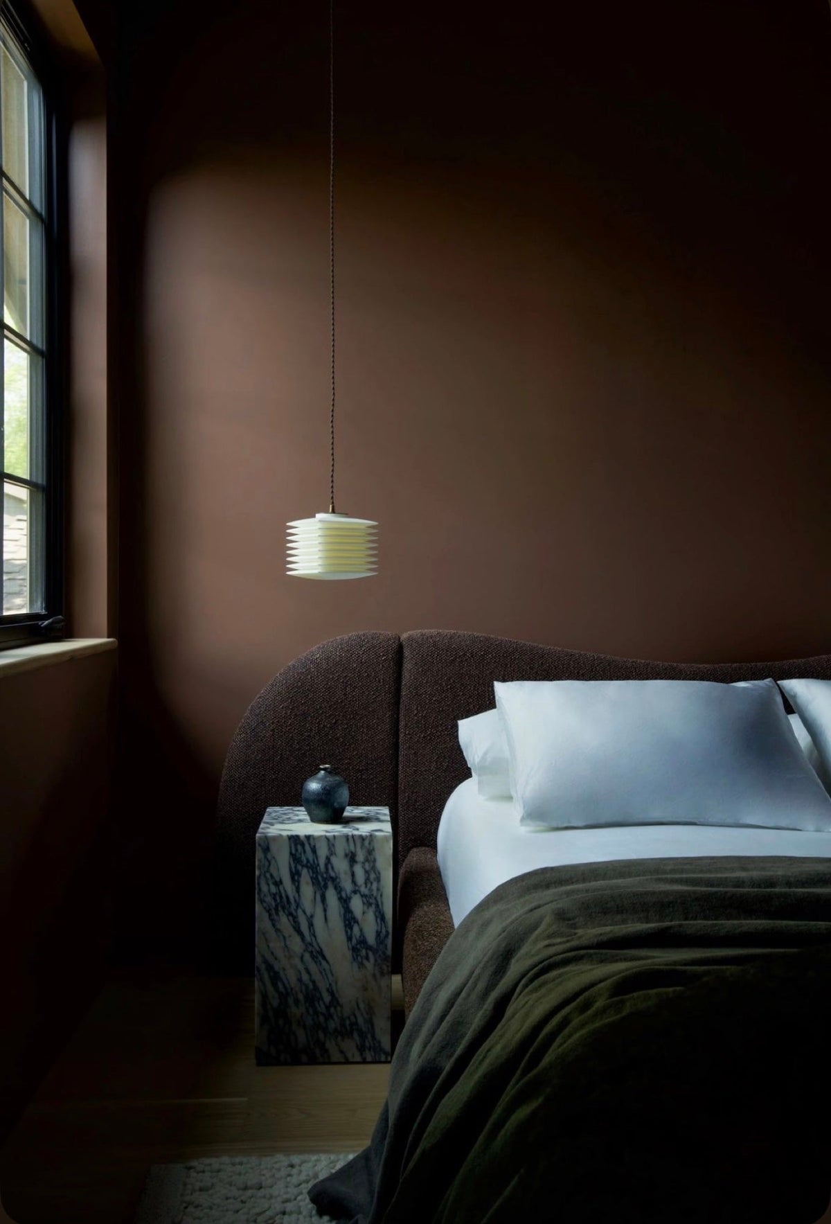 Curved bouclé bed in a deep brown bedroom with a marble side table
