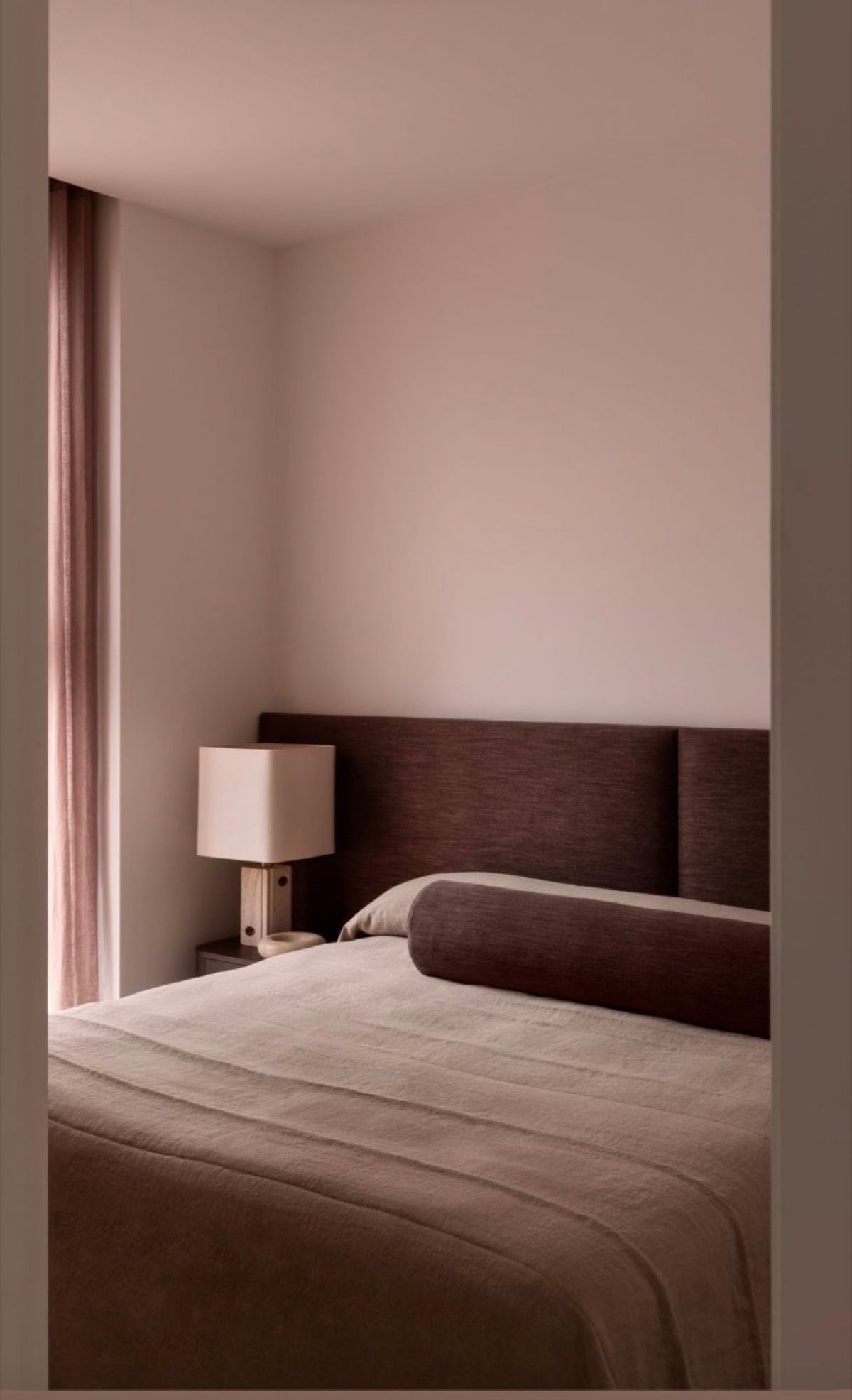 Upholstered headboard in a soft pink plastered bedroom